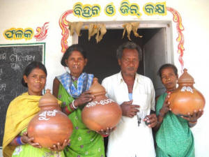 Traditional paddy seeds are labelled and stored in earthen pots at the Tentulipar community gene-seed-grain bank Picture of three women and one man holding jars containing traditional seeds.. Photo: Manipadma Jena/IPS
