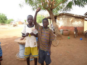 Musah Razark Adams, 13, (r) shows the sling shot that he uses to hit birds with when he works in a local rice field. Adams and his brother, Seidu, 15, (l) work to so that they can pay for school materials and levies. Credit: Albert Oppong-Ansah/IPS